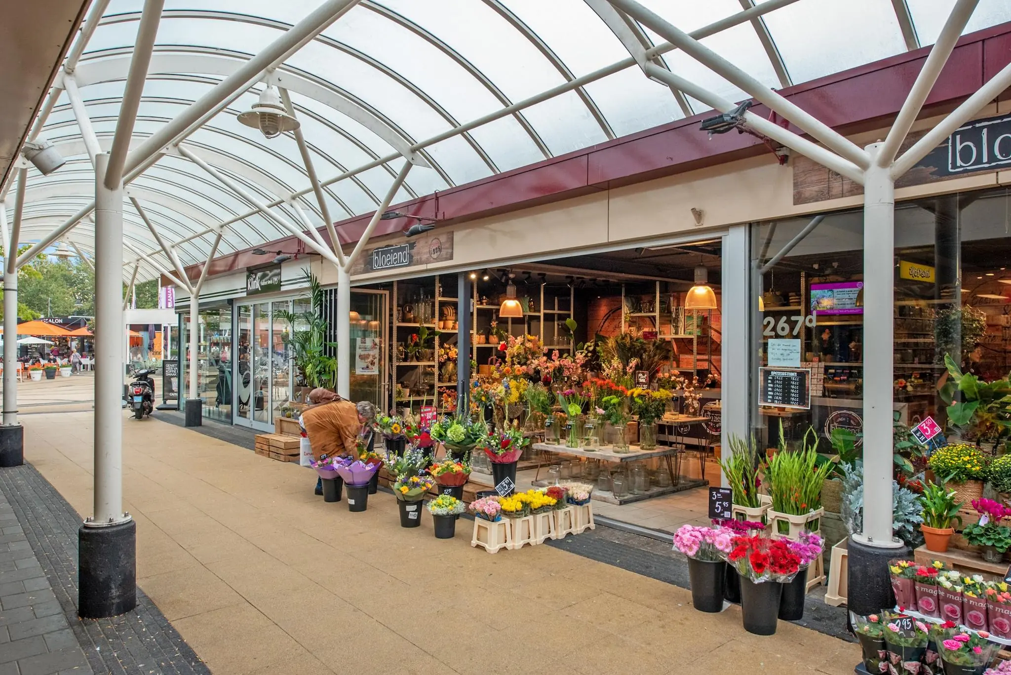 Bloemenwinkel met kleurrijke bloemen en planten onder een overdekt winkelgebied aan de Koningin Julianalaan.